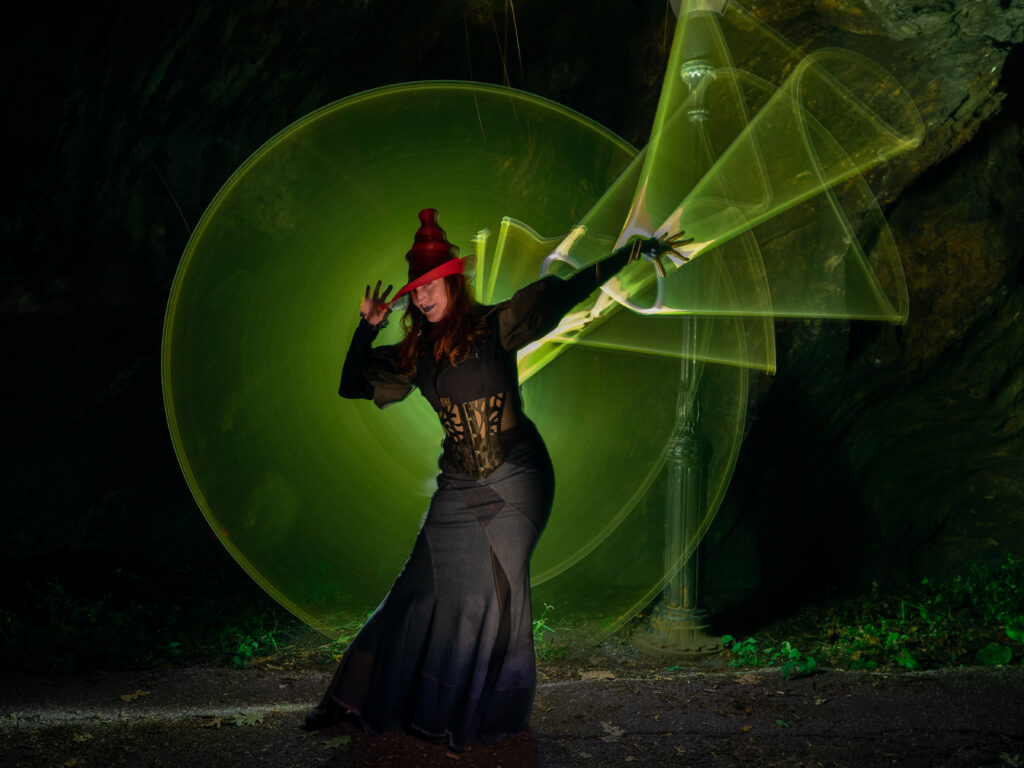 Halloween photo of a model in a witch outfit with green light painting circles and flashes