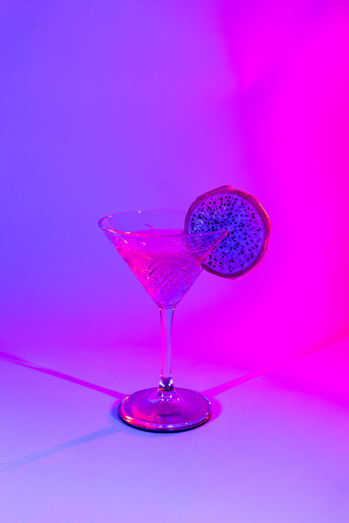A cocktail in a martini glass lit with purple and magenta lights